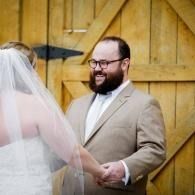 Bride and groom holding hands during an outdoor wedding ceremony before a wooden barn