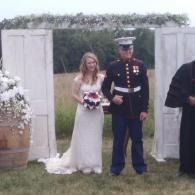 Bride and uniformed groom standing at a garden wedding arch, bride holding bouquet