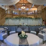 Decorated banquet hall with round tables, white chairs, and draped fabric under warm lighting