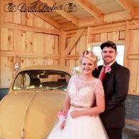 Bride and groom posing beside a vintage car in a wooden barn