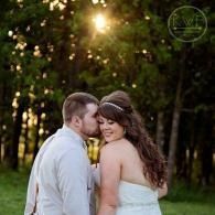Couple embracing outdoors in a sunlit forest, with the man kissing the woman’s cheek.