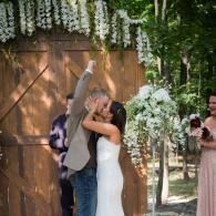 Bride and groom kiss under a floral arch at an outdoor wedding ceremony.