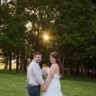 Couple holding hands in a green park at sunset, with sun shining through the trees.