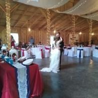 Bride in white dress standing in a decorated banquet hall with red-draped tables and string lights
