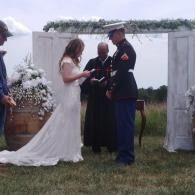 Bride and groom standing with an officiant during an outdoor wedding ceremony under an arch