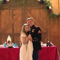 Couple in dress and military uniform posing at a reception table in front of rustic barn doors