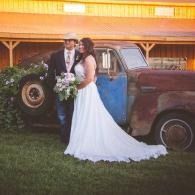 Bride and groom posing beside a vintage blue-and-rust truck at sunset