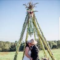 Couple kissing beneath a tall floral teepee in a sunny field