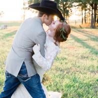 Couple in cowboy hat and white dress kissing in a sunlit grassy field