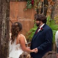 Bride and groom holding hands during an outdoor wedding ceremony in front of a wooden backdrop