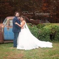 Bride and groom posing in a garden beside a blue vintage truck, bride in a white gown