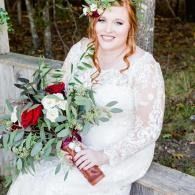 Woman in a white lace dress holding a bouquet of red and white flowers outdoors.