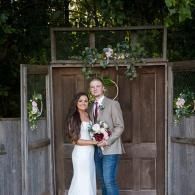 Bride and groom posing in front of rustic wooden doors with floral decor