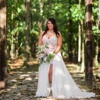 Woman in a white gown holding a bouquet in a sunlit forest setting.