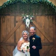 Wedding couple posing in front of rustic wooden barn doors with floral arch backdrop