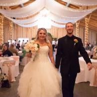 Bride and groom walking down a decorated wedding reception aisle, smiling and holding hands