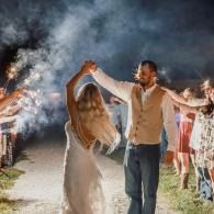 Couple dancing outdoors at night amid sparklers and smoke, with guests watching in the background