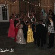 People dancing at a dimly lit indoor party, with a woman in a gold dress at center.