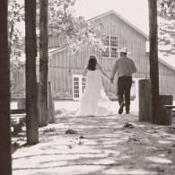 Couple holding hands, walking toward a barn in a snowy wooded setting