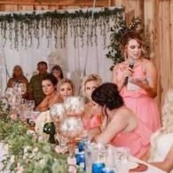 Woman in a pink dress speaking at a decorated banquet table with guests seated nearby