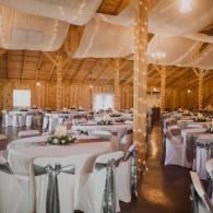 Elegant banquet hall with round white-tablecloth tables, silver chairs, and draped fabric ceiling accents
