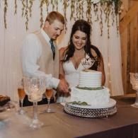 Couple cutting a white tiered wedding cake at a reception table with champagne glasses nearby