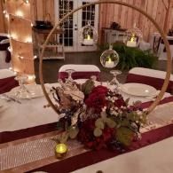 Elegant table centerpiece with gold hoop, red flowers, candles, and table settings in a warmly lit reception hall