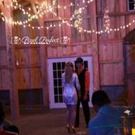 Couple dancing outdoors under string lights beside a rustic wooden barn at night