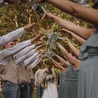 Raised hands holding a flower wreath overhead in an outdoor celebration under autumn trees