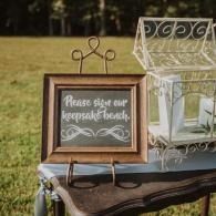 Sign our keepsake bench sign beside a white decorative card box on a table outdoors