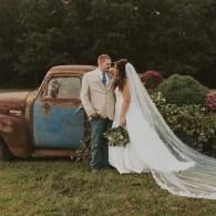 Bride and groom kissing beside a rusted vintage truck in a grassy field