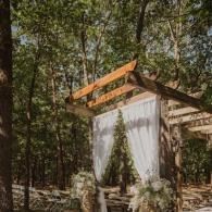 Small forest shelter with a white curtain and wooden roof in a wooded area