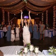 Woman in white dress celebrates with arms raised at a decorated indoor event reception