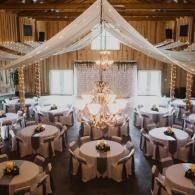 Elegant dining hall set for a formal event, with round tables, chandeliers, and white draped ceiling decor