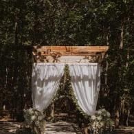 Outdoor wedding arch with white drapes and floral arrangements in a wooded setting
