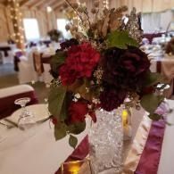 Floral centerpiece with burgundy and red flowers on a banquet table in a decorated reception hall