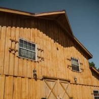 Wooden barn exterior with two windows and large double doors under a slanted roof.