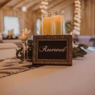Reserved sign on a table at a warmly lit event venue, with candles and floral decor in the background