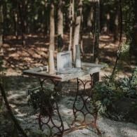 Wooden table with a mirror in a wooded outdoor setting, surrounded by trees and plants.
