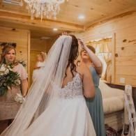 Bride being adjusted in a cozy wooden room while bridesmaids assist before the ceremony