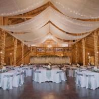 Elegant banquet hall with draped white fabric and round tables set for a reception