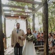 Bride and groom walking down a decorated outdoor aisle beneath hanging glass lanterns
