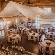 Elegant barn wedding reception with round tables, white drapes, and warm candlelight