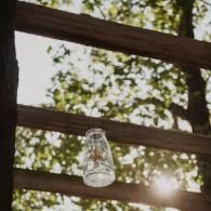 Glass jar hanging from a wooden railing with sunlight filtering through trees behind it