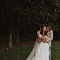 Two people embracing in white clothing in a dark, wooded outdoor setting