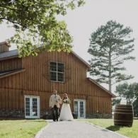 Bride and groom walking down a path beside a rustic barn venue