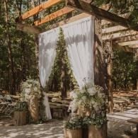 Rustic outdoor wedding arch with white drapery and greenery under a wooden pergola