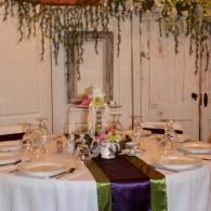 Elegant banquet table with white linens, greenery, flowers, and purple and green runner decor