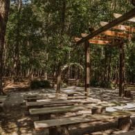 Outdoor stone picnic tables beneath a wooden pavilion in a wooded park