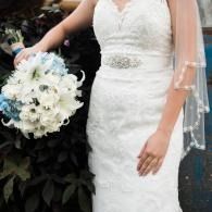 Bride in white lace wedding dress holding a white bouquet with veil